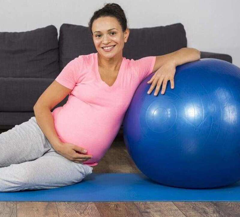 mujer embarazada sonriente en casa con colchoneta de ejercicios con pelota