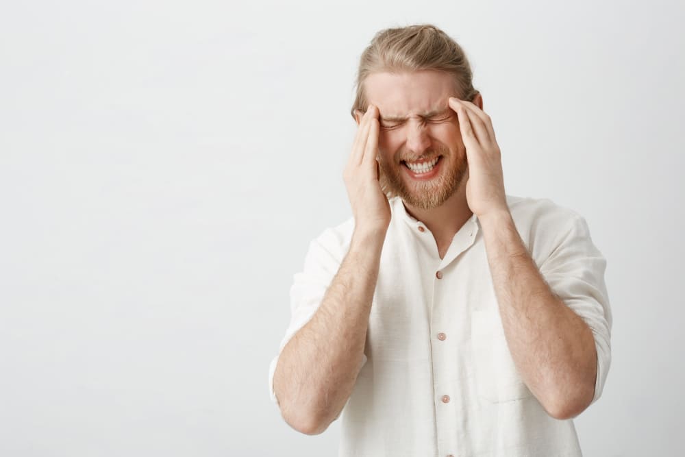 hombre con las manos en la cabeza con expresion de molestia o dolor en fondo blanco
