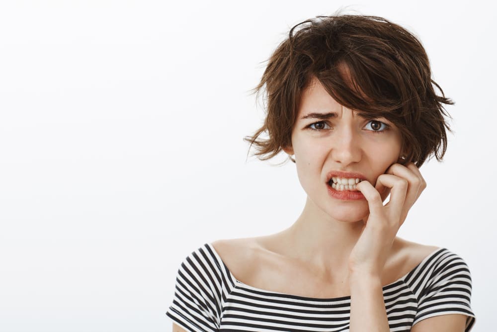 mujer con gesto de incomodidad sujetandose la cara en fondo blanco
